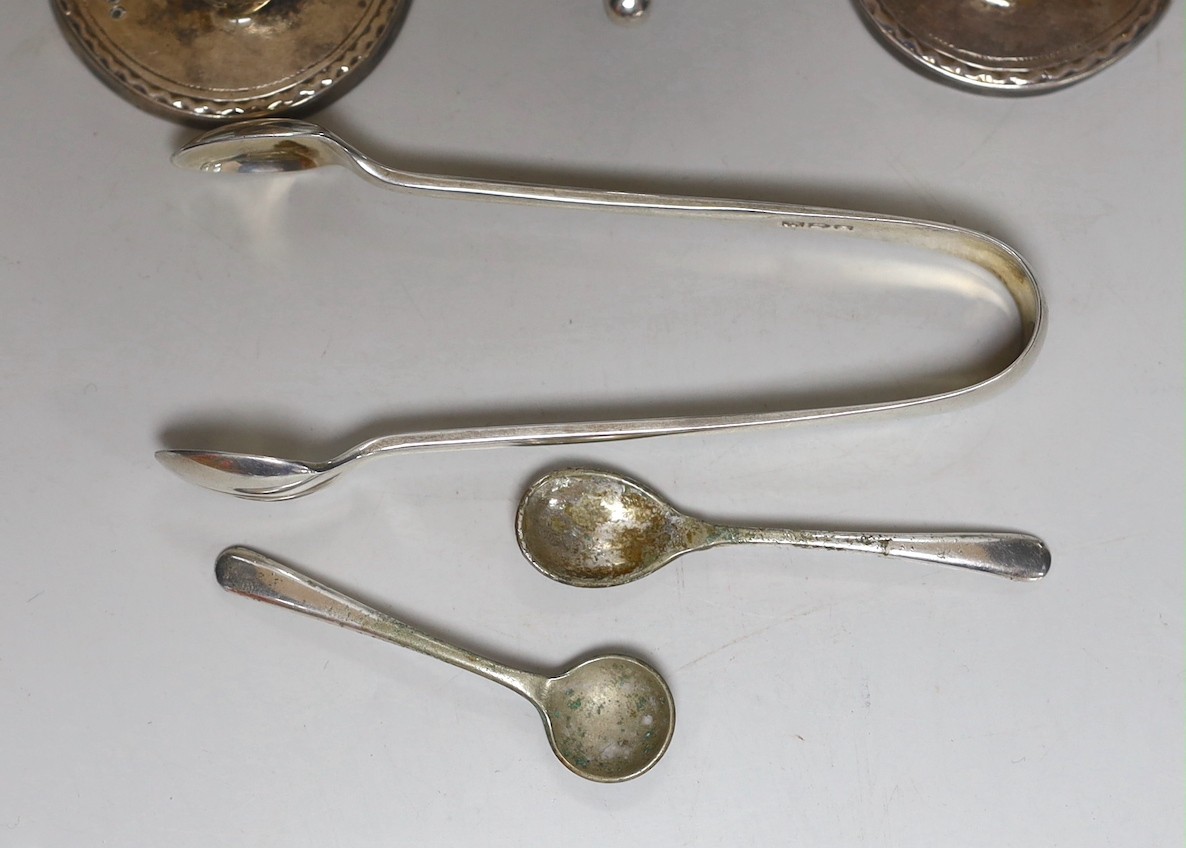 A pair of George V silver two handled boat shaped pedestal salts length 10.7cm, a pair of Edwardian silver pepperettes, a pair of late Victorian silver menu holders, a pair of silver sugar tongs and a three piece plated